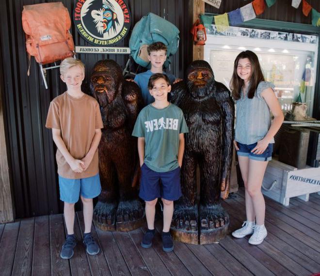 children standing next to carved statues of Bigfoot